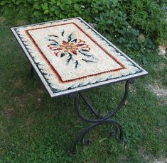 a mosaic table sitting on top of a lush green grass covered field next to bushes