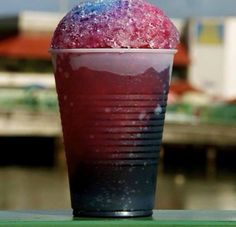 a red drink sitting on top of a green table next to a body of water