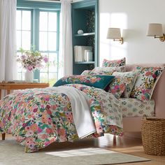 a bed with floral comforter and pillows in a room next to a window,