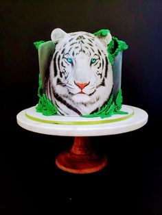 a white tiger cake with green icing on a pedestal in front of a black background