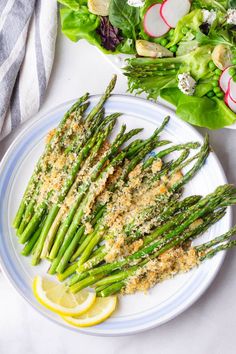 grilled asparagus with parmesan and lemon on a white plate next to salad