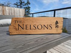 a wooden sign that says the nelsons sitting on a table next to a lake