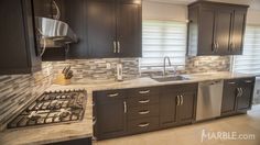 a kitchen with dark wood cabinets and marble counter tops, stainless steel appliances and sink