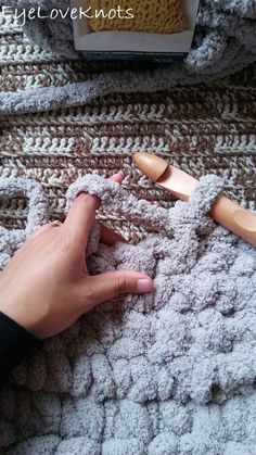 someone is crocheting on the blanket with their hand and wooden spoons next to them