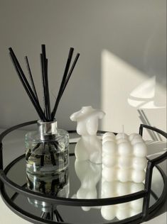 a glass table topped with candles next to a vase filled with liquid and reeds