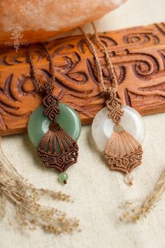 two necklaces with different designs on them sitting on a piece of wood next to a rock