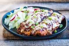 a black plate topped with meat covered in gravy next to a pile of salad