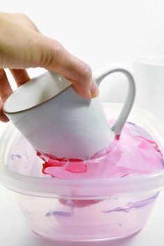 a person pours liquid into a plastic container with a white cup in it and another hand is holding the lid