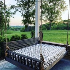 a wooden swing bed sitting on top of a stone patio next to a lush green field