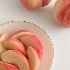 sliced peaches in a bowl on a white surface next to two pieces of fruit