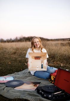 a woman sitting on a blanket holding up a laptop