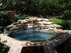 an outdoor hot tub in the middle of a garden with rocks and water flowing from it