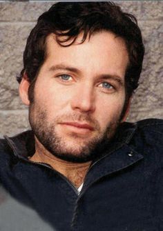 a man sitting in front of a brick wall looking at the camera with a serious look on his face