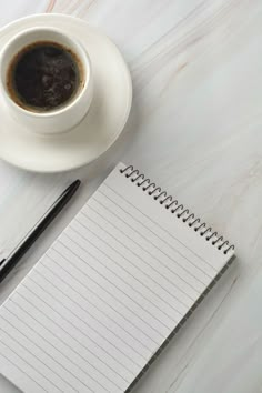 a cup of coffee next to a notepad and pen on a white table top