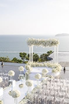 an outdoor wedding setup with white flowers and candles on the table next to the ocean