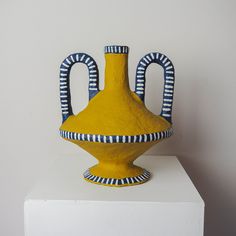 a yellow and blue vase sitting on top of a white pedestal next to a wall