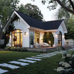 a small white house with black roof and windows on the front porch is lit up at night