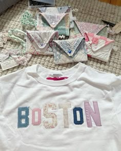 the boston t - shirt is laying on the bed next to many pieces of fabric