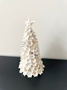 a small white christmas tree made out of seashells on a black countertop