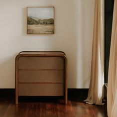 a brown dresser sitting next to a window in a room with wooden floors and white walls