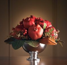 a silver bowl filled with pomegranates and leaves on top of a wooden table