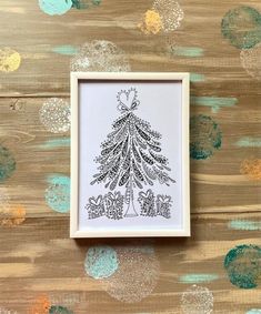 a black and white christmas tree in a frame on top of a wooden table with confetti