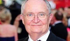 an older man in a suit and tie smiling at the camera with other people behind him