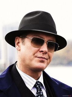 a man in a suit and tie wearing a black hat with sunglasses on his face