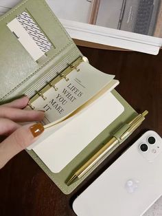 a person is holding an open book next to their cell phone and other items on the table