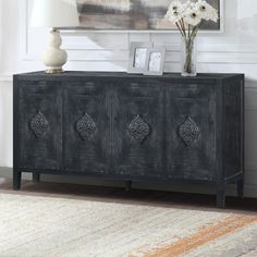 a black sideboard with ornate carvings on the doors and drawers in front of a white wall