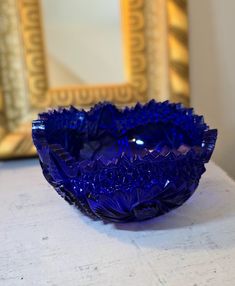 a blue glass bowl sitting on top of a white table next to a gold framed mirror