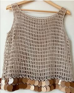 a crochet top with buttons hanging on a wooden hanger