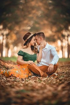 a man and woman sitting on the ground in front of trees with leaves around them