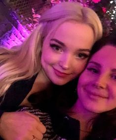 two women are taking a selfie in front of a purple light at a party