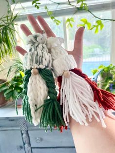 the hand is holding three different knitted objects in it's palm, and there are green leaves on the window sill