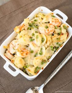 a casserole dish with shrimp, peas and cheese in it next to a spoon