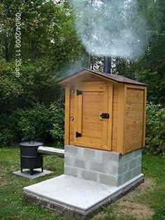 a small wooden outhouse sitting on top of a cement block next to a trash can