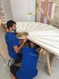 two men in blue shirts working on a large fan