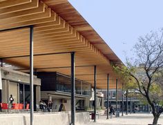 people are sitting on benches in front of a building with wooden slatted roof