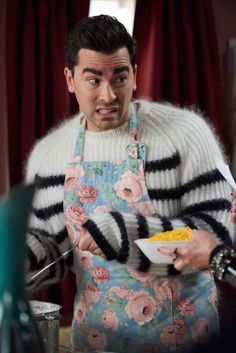 a man in an apron holding a bowl of food and looking surprised at the camera