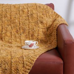 a cup and saucer sitting on top of a brown chair next to a blanket