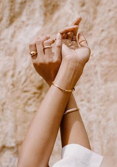 a woman is holding her hand up in front of a stone wall and wearing gold bracelets