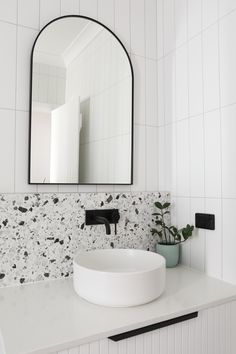 a white sink sitting under a large mirror in a bathroom next to a potted plant