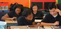 four students are sitting at desks with their ipads and looking at the screen