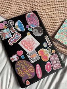 two notebooks with stickers on them sitting on a bed next to each other