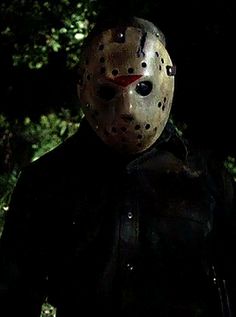 a person wearing a mask standing in the dark with trees behind them and one hand on his hip