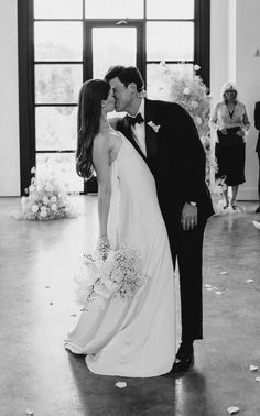 a bride and groom kissing in front of an open doorway with petals on the floor