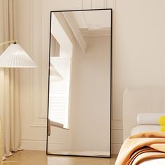 a large mirror sitting on top of a wooden floor next to a lamp and bed