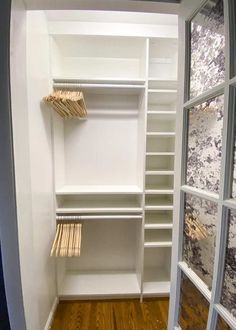 an empty walk - in closet with white shelves and wood flooring is seen through the open door