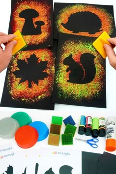 someone is painting silhouettes on black paper with yellow and green paint, while another person holds a sponge